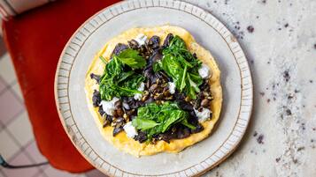 Un plato de comida con vegetales, hongos y queso sobre una fuente de cerámica.