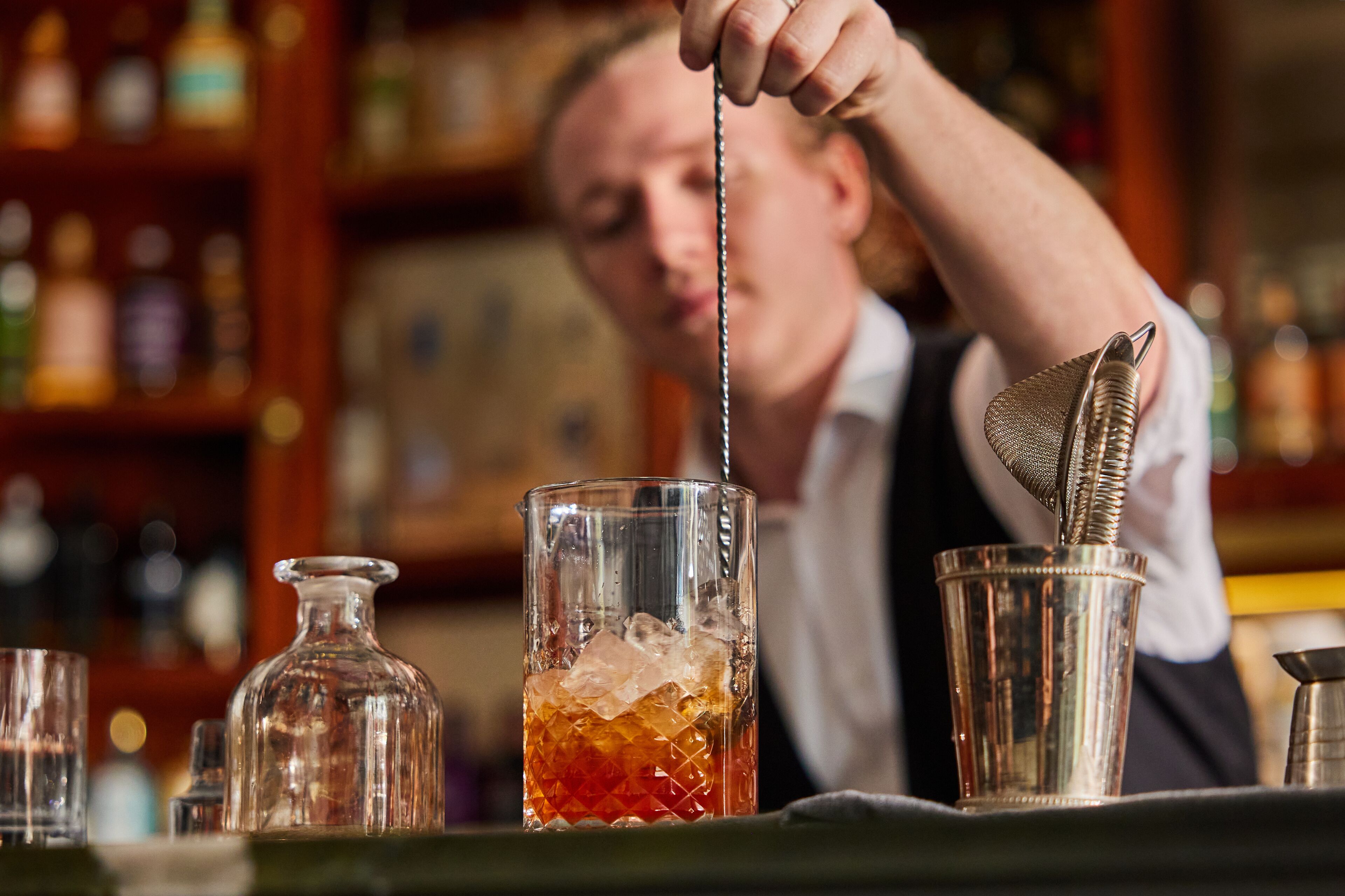 A bartender preparing a drink with a shaker and a glass.