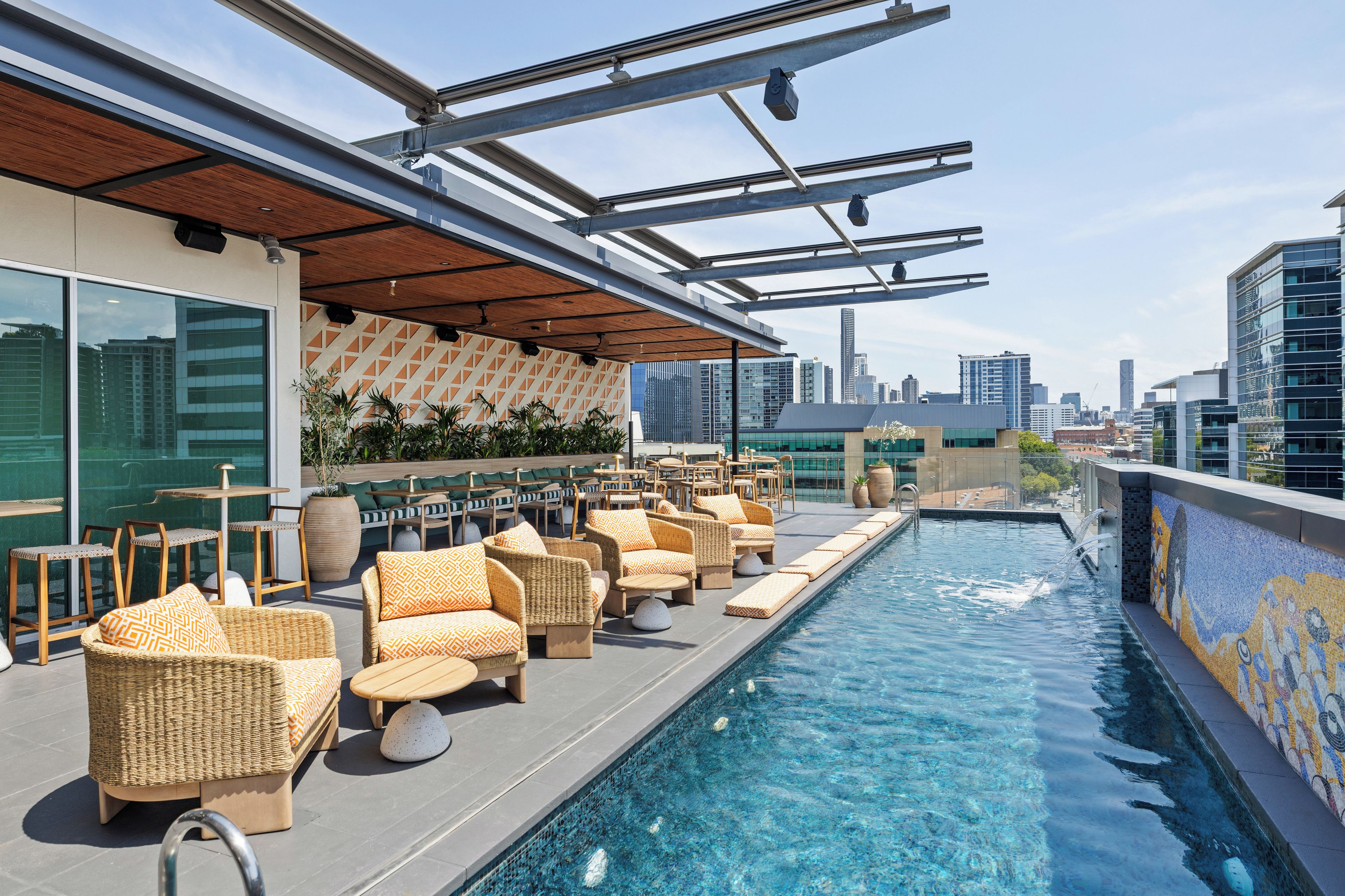 A rooftop pool area with lounge chairs and a city skyline view.