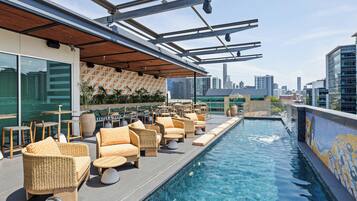 A rooftop pool area with lounge chairs and a city skyline view.