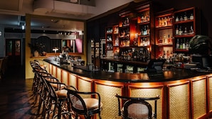 A bar area with a counter, bar stools, and shelves stocked with bottles.