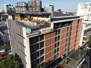 Et moderne hotel med loungeområde på taget, store vinduer og et tydeligt 'Ovalo Hotels' skilt.