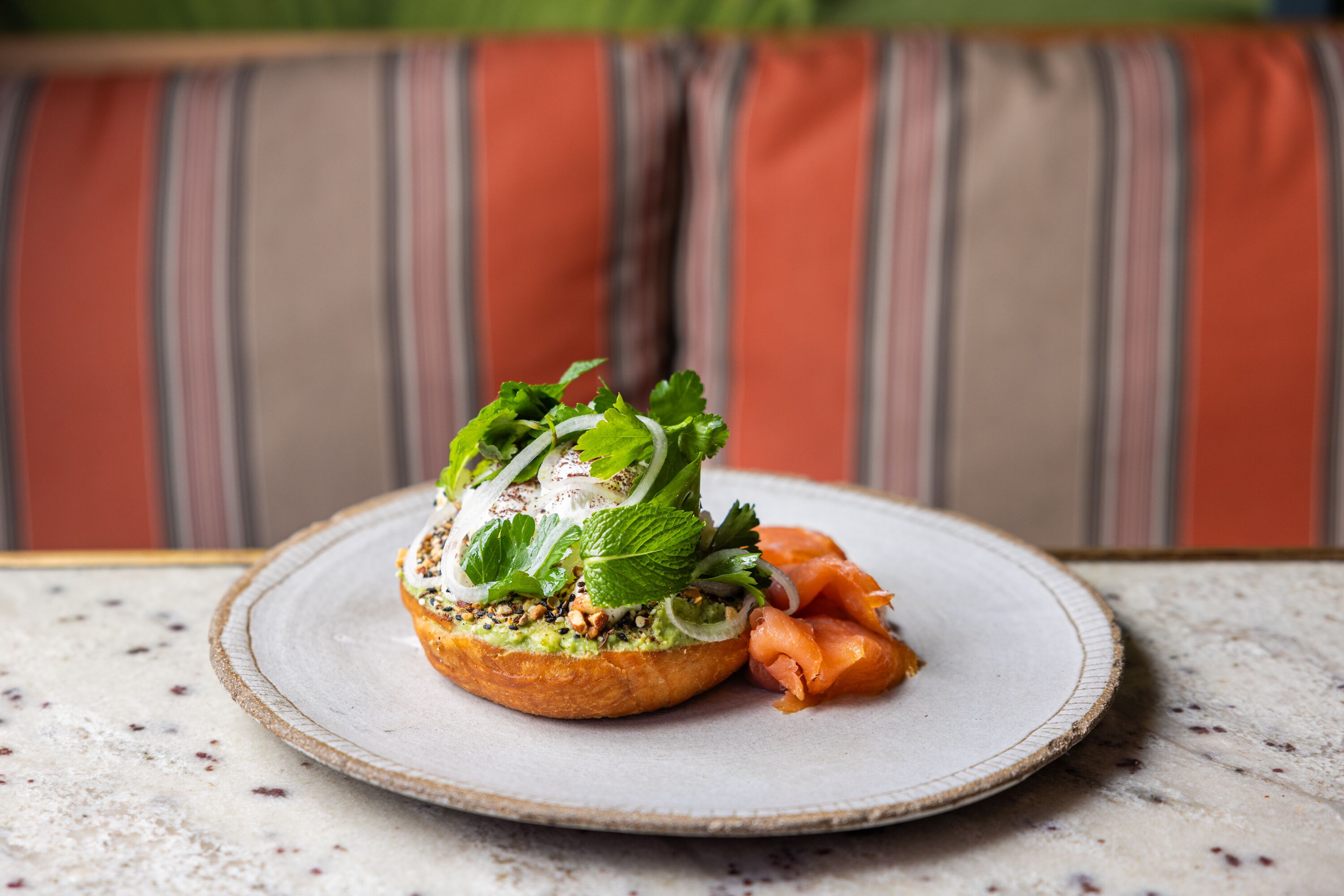 A plate with a sandwich and smoked salmon on a speckled table.