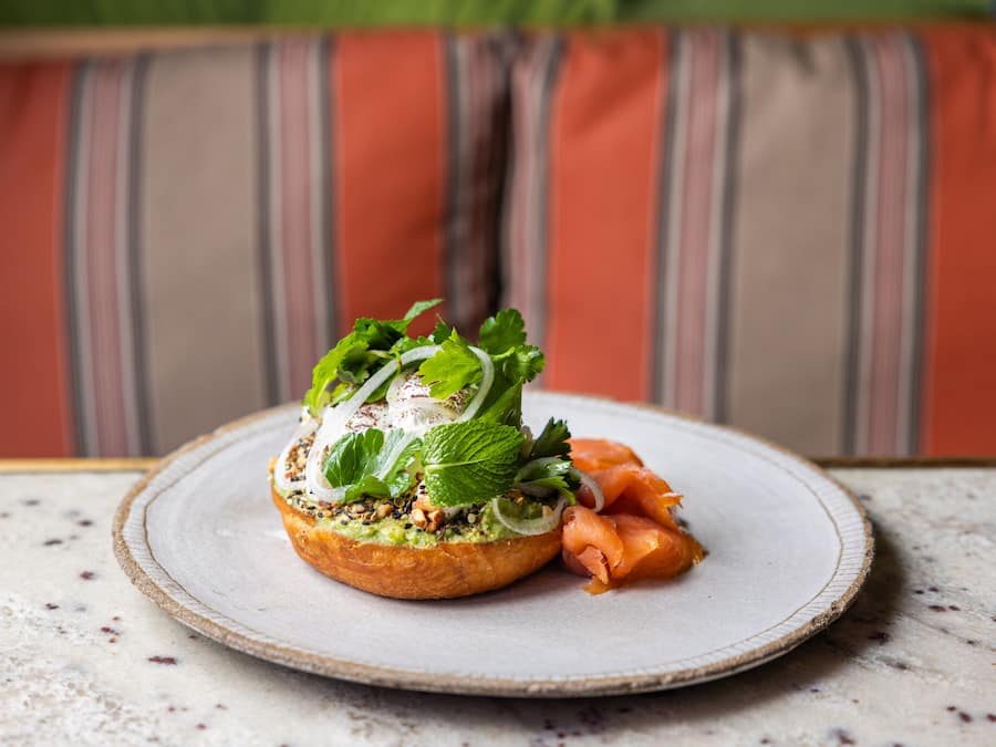 A plate with a sandwich and smoked salmon on a speckled table.