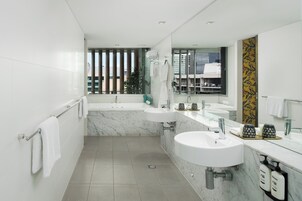 A modern bathroom with a large mirror, two sinks, a bathtub, and a window with a city view.