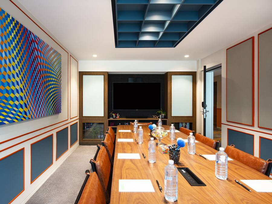 Un salón de conferencias con una larga mesa, sillas, botellas de agua y una pantalla grande.