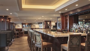 A bar area with a long counter, multiple stools, and a wall of liquor bottles.