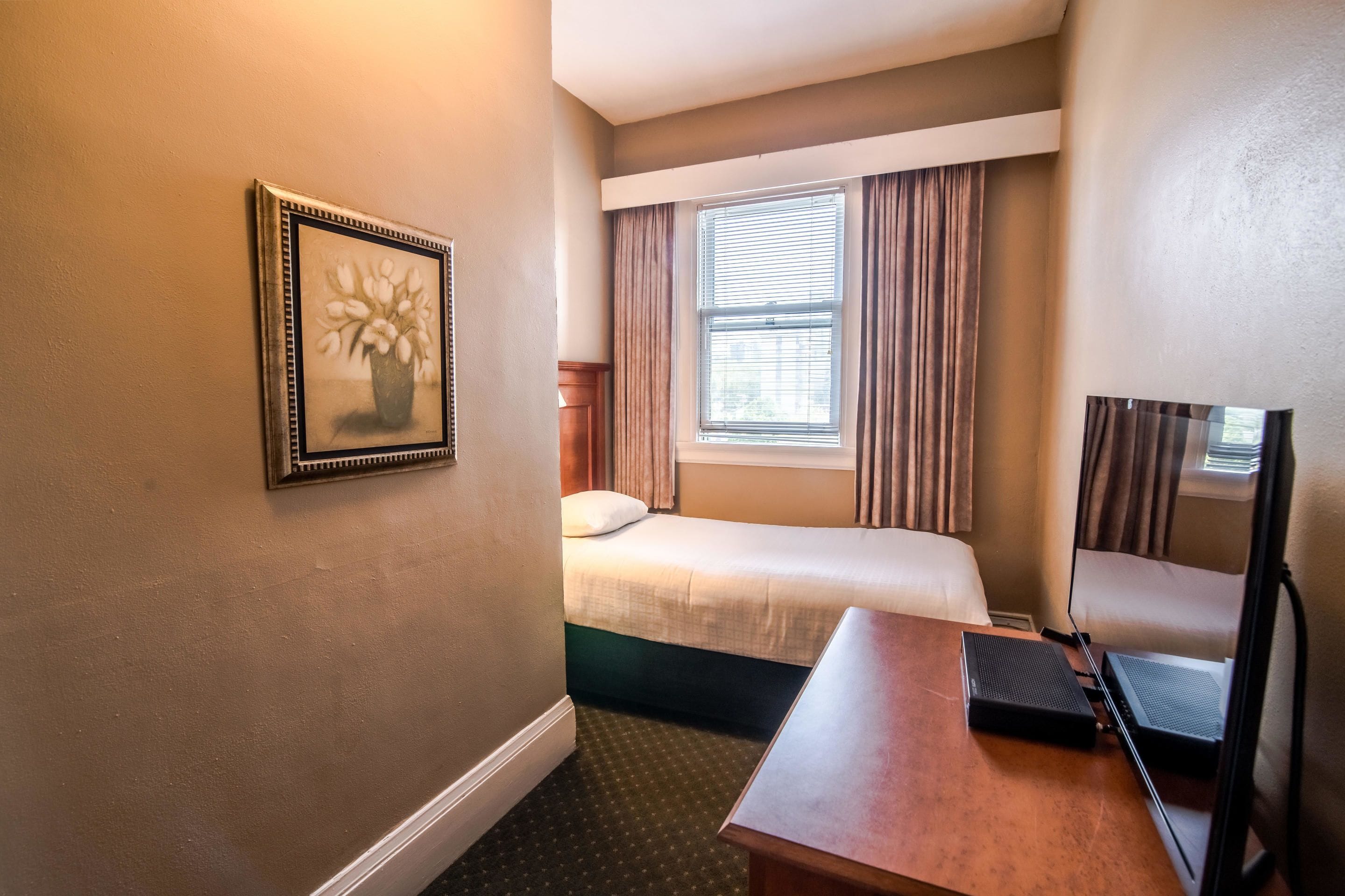 A hotel room with a bed, a desk, a chair, a TV, and a window with curtains.
