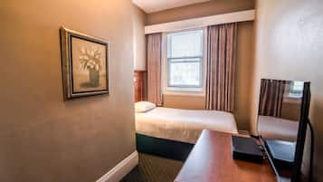 A hotel room with a bed, a desk, a chair, a TV, and a window with curtains.
