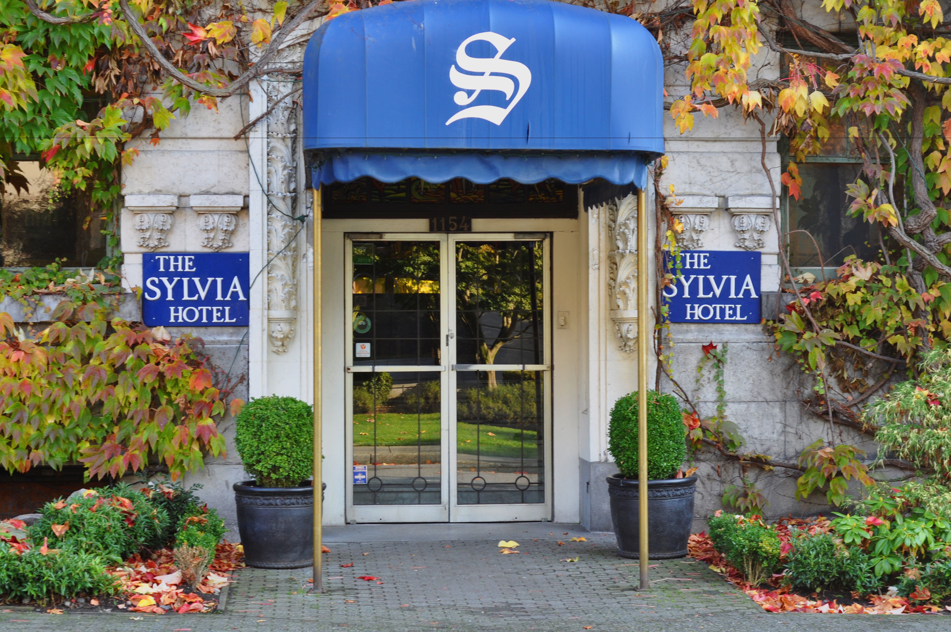 The entrance of The Sylvia Hotel with a blue awning, double doors, and potted plants.