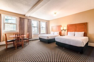 A hotel room with two beds, a wooden chair, a small table, and a patterned carpet.
