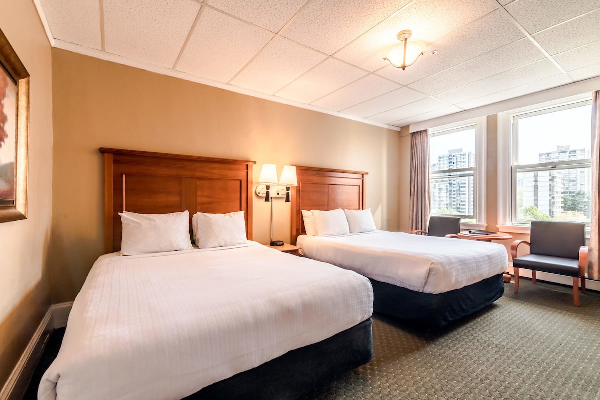 A hotel room with two beds, a desk, a chair, and a window with a city view.