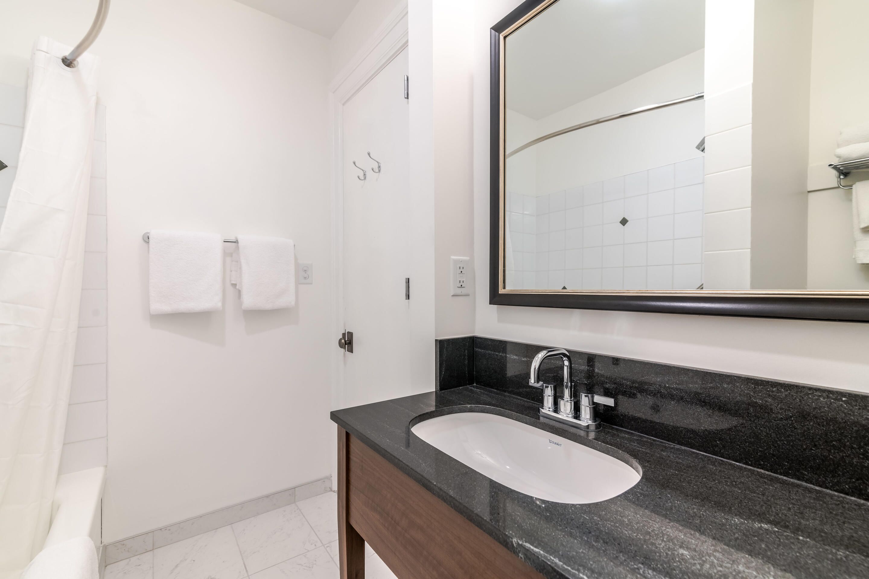 Baño con lavamanos blanco, encimera oscura y un espejo grande.