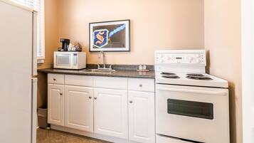 A compact kitchen with white cabinets, a microwave, a sink, and a stove.