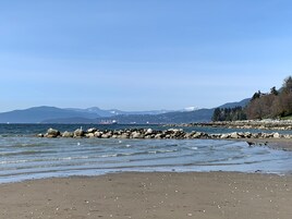 A beach with rocky shoreline, calm water, and distant mountains.
