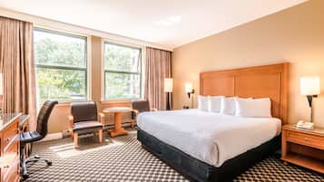 Habitación de hotel con una cama grande, dos sillas, un escritorio, una lámpara y una ventana con cortinas.