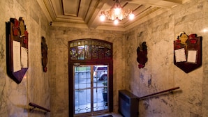 A marble-floored entrance with a glass door, a chandelier, and a staircase with a handrail.