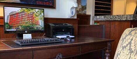 Un hall de hotel con un escritorio de madera, una computadora, una impresora y un sillón con estampado.