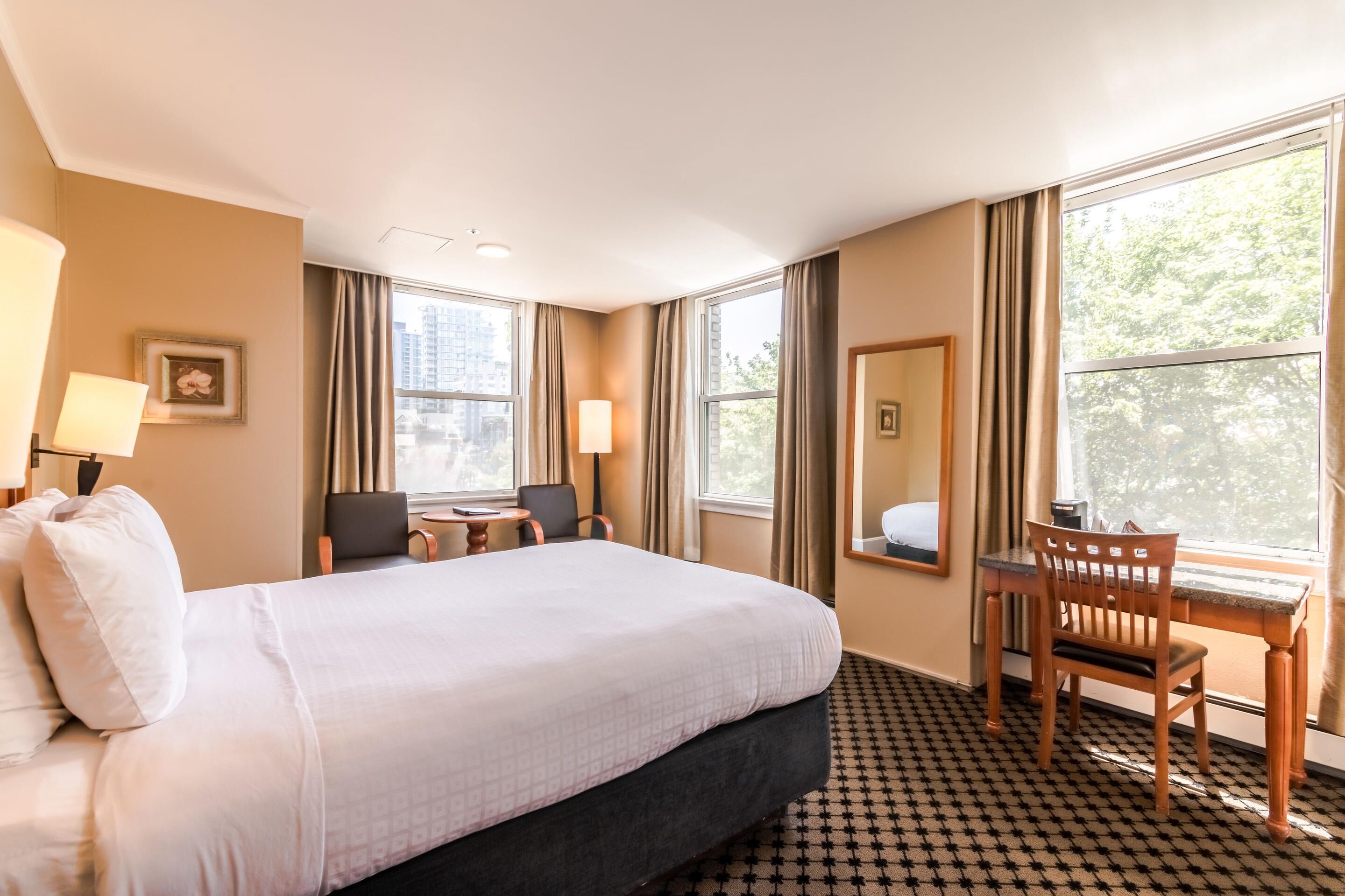 A hotel room with a large bed, a desk with a chair, a small table, and a window with curtains.