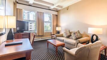 A hotel room with a sofa, armchairs, a TV, a desk, and a patterned carpet.
