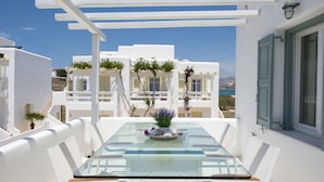 A glass-top table with white chairs, a potted plant, and a bowl of fruit. - Corfos Hotel (Mykonos)