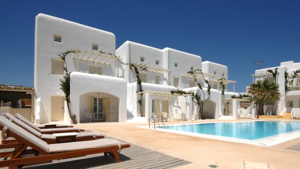 A poolside area with white buildings, lounge chairs, and a clear blue sky. - Corfos Hotel (Mykonos)