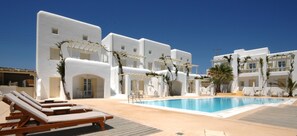 Zona de piscina amb edificis blancs, gandules i un cel blau clar.
