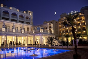 A hotel with a pool, multiple balconies, and a crescent moon in the sky.