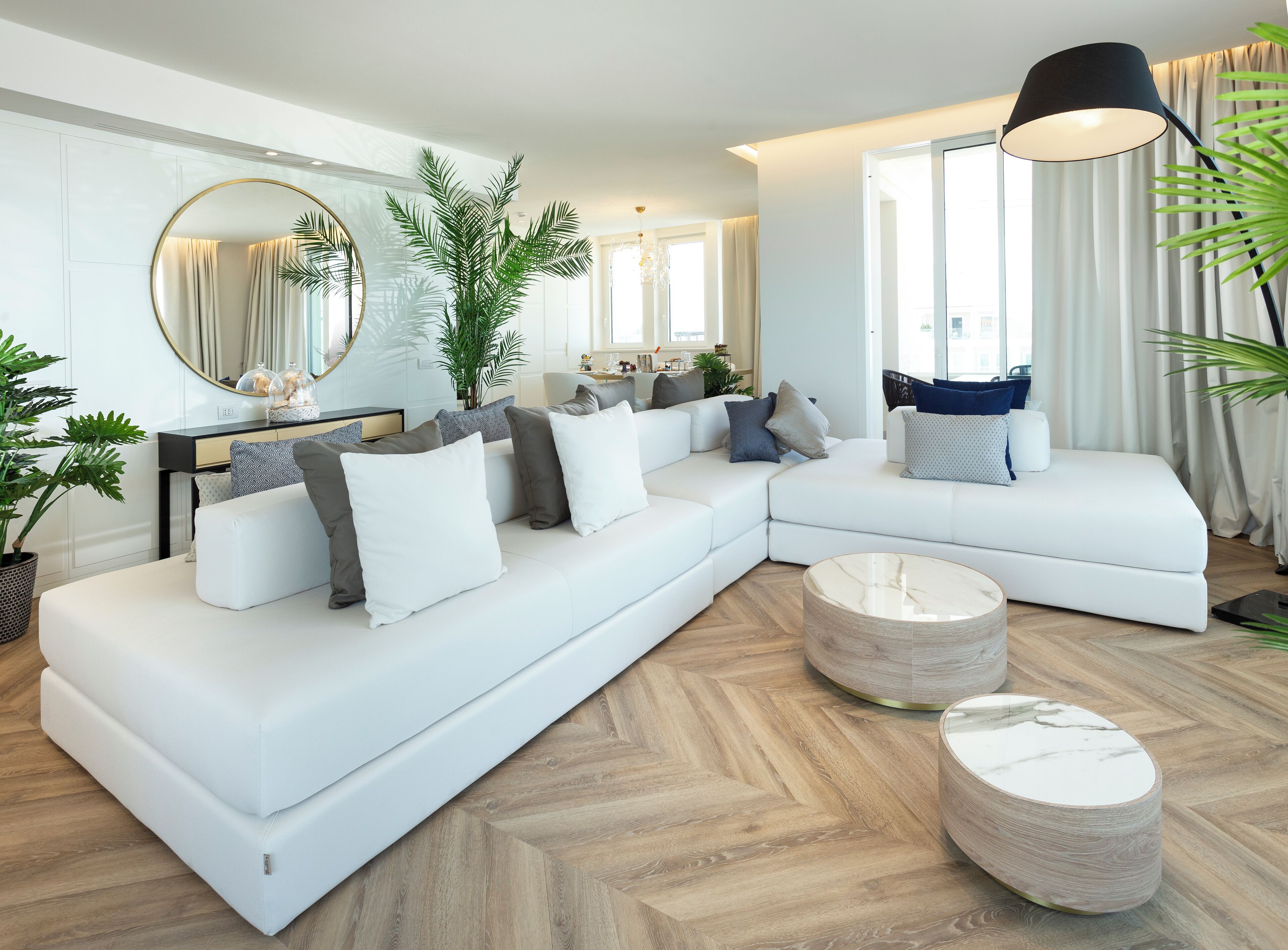 A modern living room with a white sectional sofa, a round coffee table, and a large mirror.