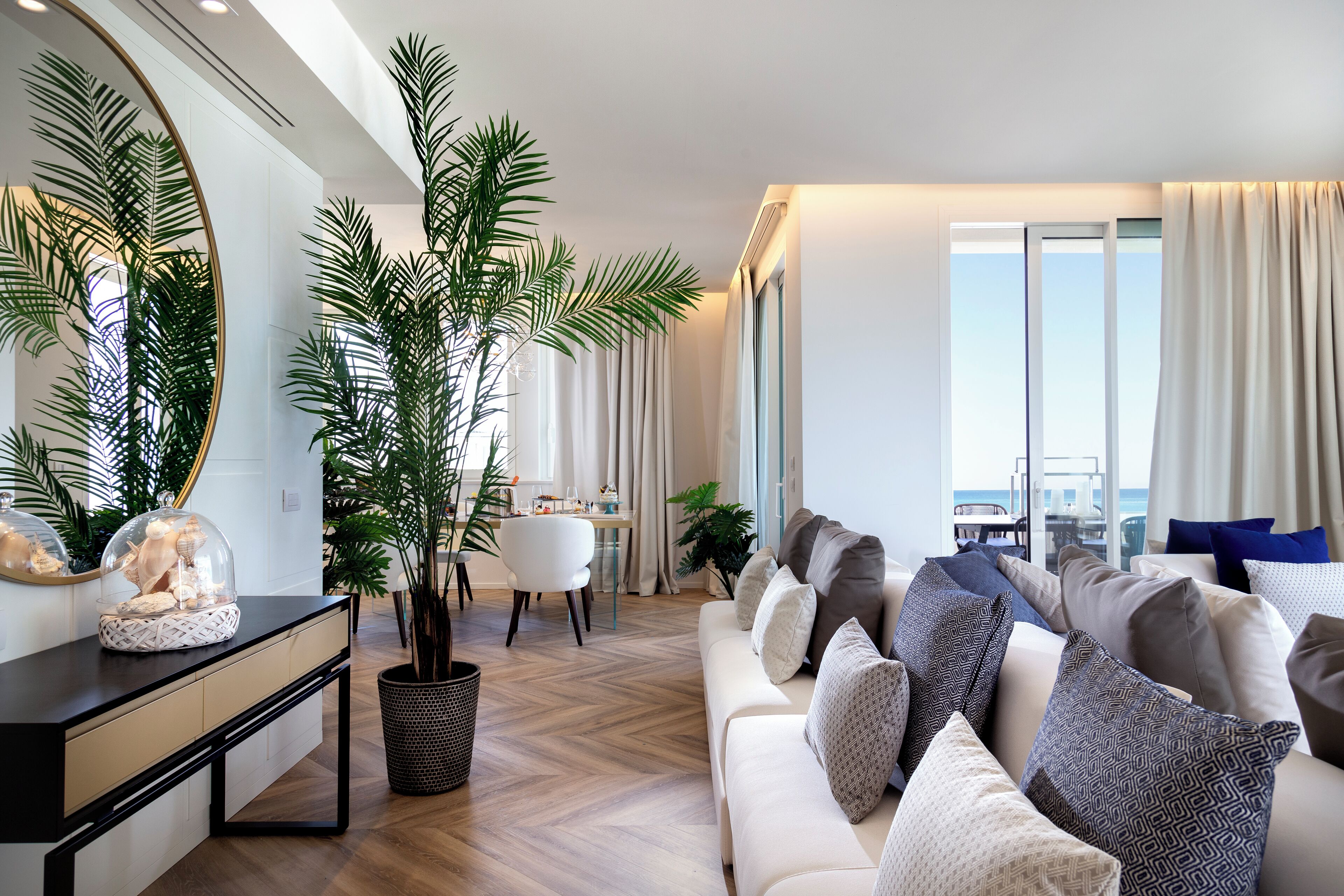 A modern living room with a sofa, a dining table, and a large window with curtains.