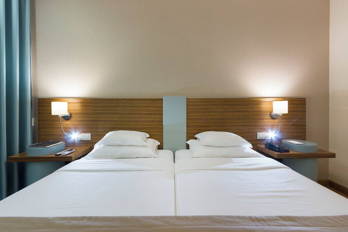 A hotel room with two beds, each with a bedside table, lamp, and telephone.