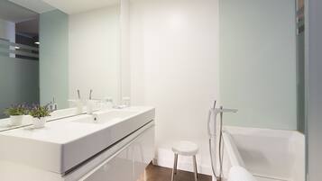 Un baño moderno con un espejo grande, dos lavamanos, una bañera blanca y un taburete pequeño.