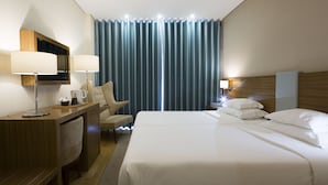Habitación de hotel con una cama grande, un escritorio con silla, televisión y mesita de noche con lámpara.