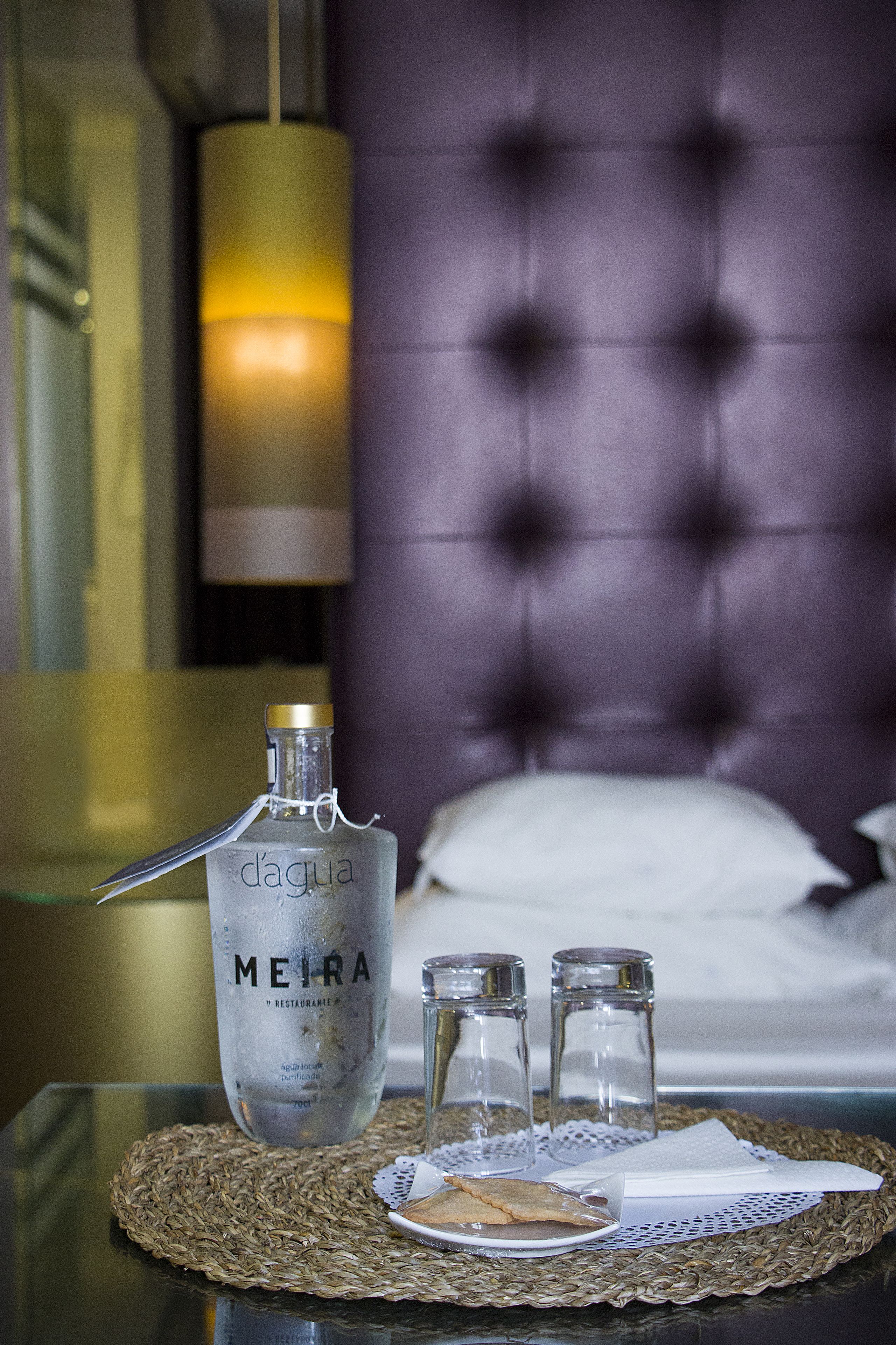 En minibar med en flaske Dagua MEIRA, to salt- og peberkværke samt en tallerken med serviet og en kiks på en vævet underlag.