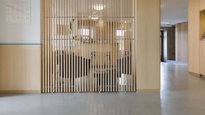 Un interior moderno con un separador de madera, luces empotradas en el techo y un área de oficina visible con escritorios y sillas.