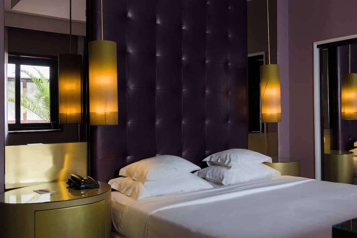 A hotel room with a tufted headboard, a bedside table with a telephone, and a bed with white bedding.