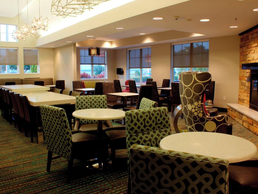 Uma sala de jantar de hotel com várias mesas e cadeiras, grandes janelas e uma lareira.