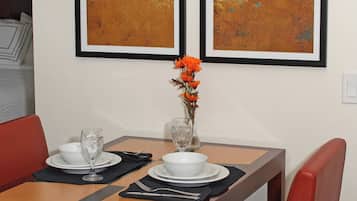 A dining table set with white plates, glasses, and a vase with orange flowers. Two abstract paintings hang on the wall above the table.