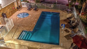 Une piscine rectangulaire dotée d’un plongeoir, entourée de chaises longues et de parasols, et une terrasse en briques.