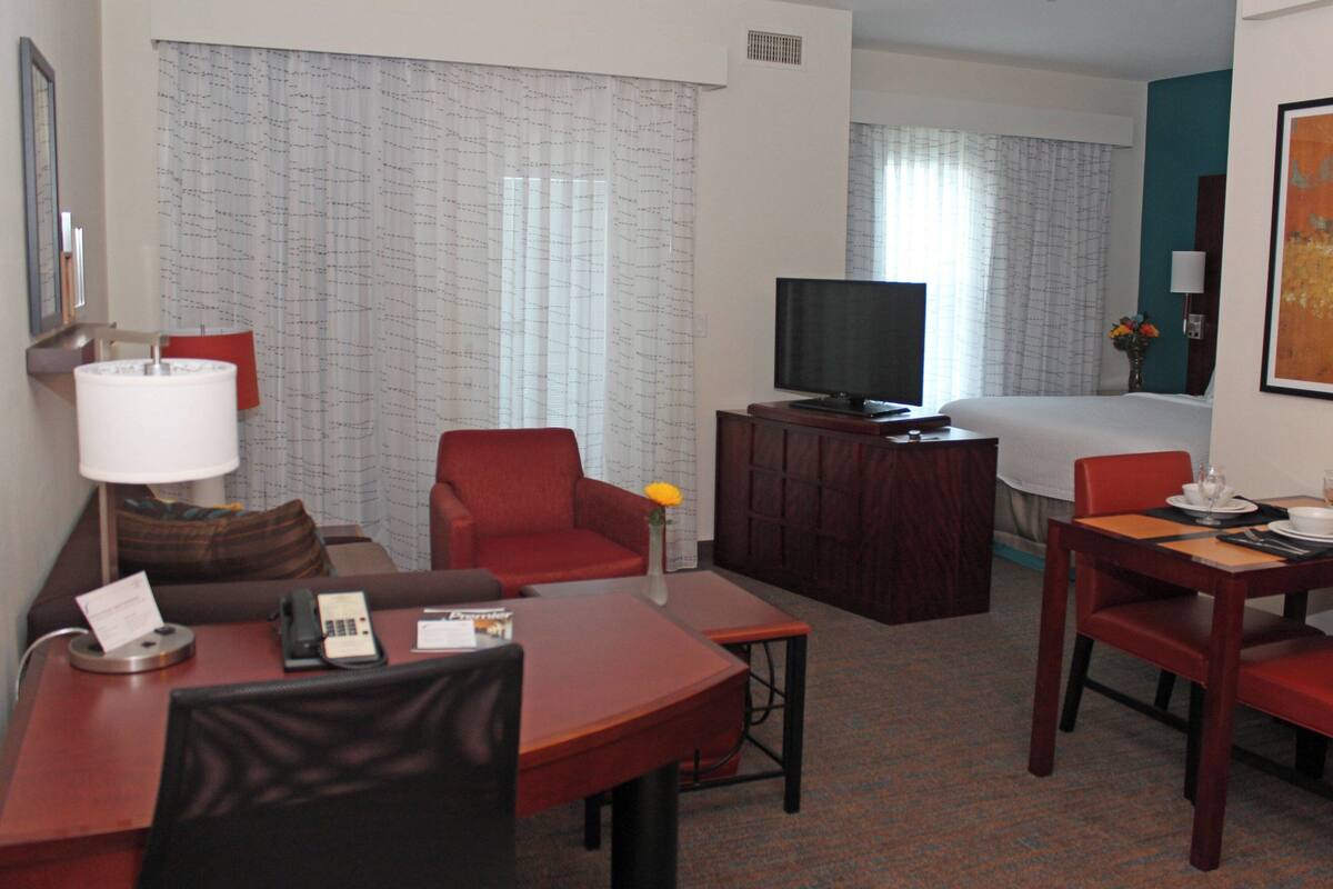 A hotel room with a bed, a TV, a desk with a telephone, and a dining area with chairs and a table.
