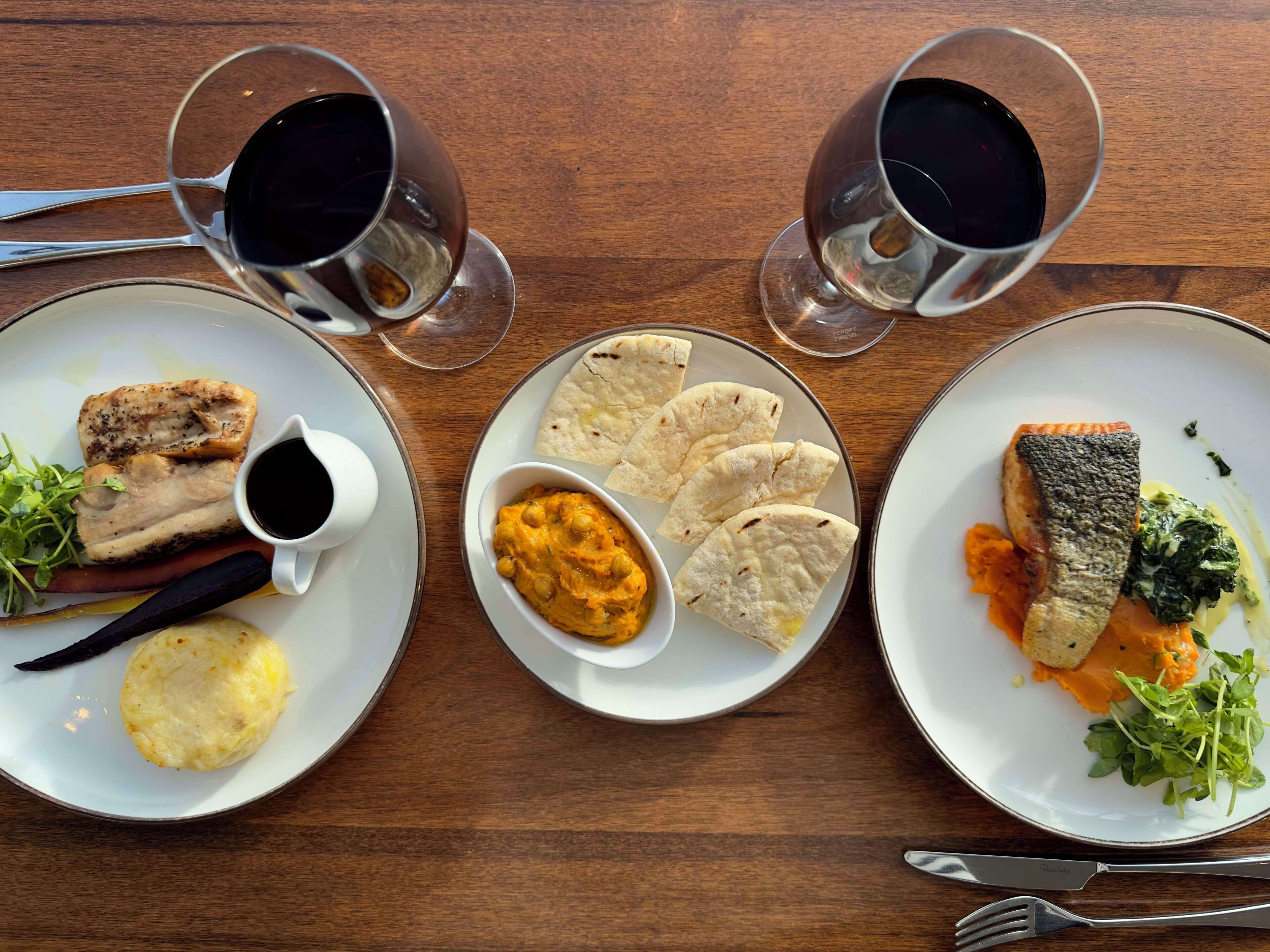 Three plates of food with two glasses of black beverage on a wooden table.