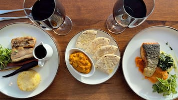 Trois assiettes de nourriture et deux verres d’une boisson noire sur une table en bois.