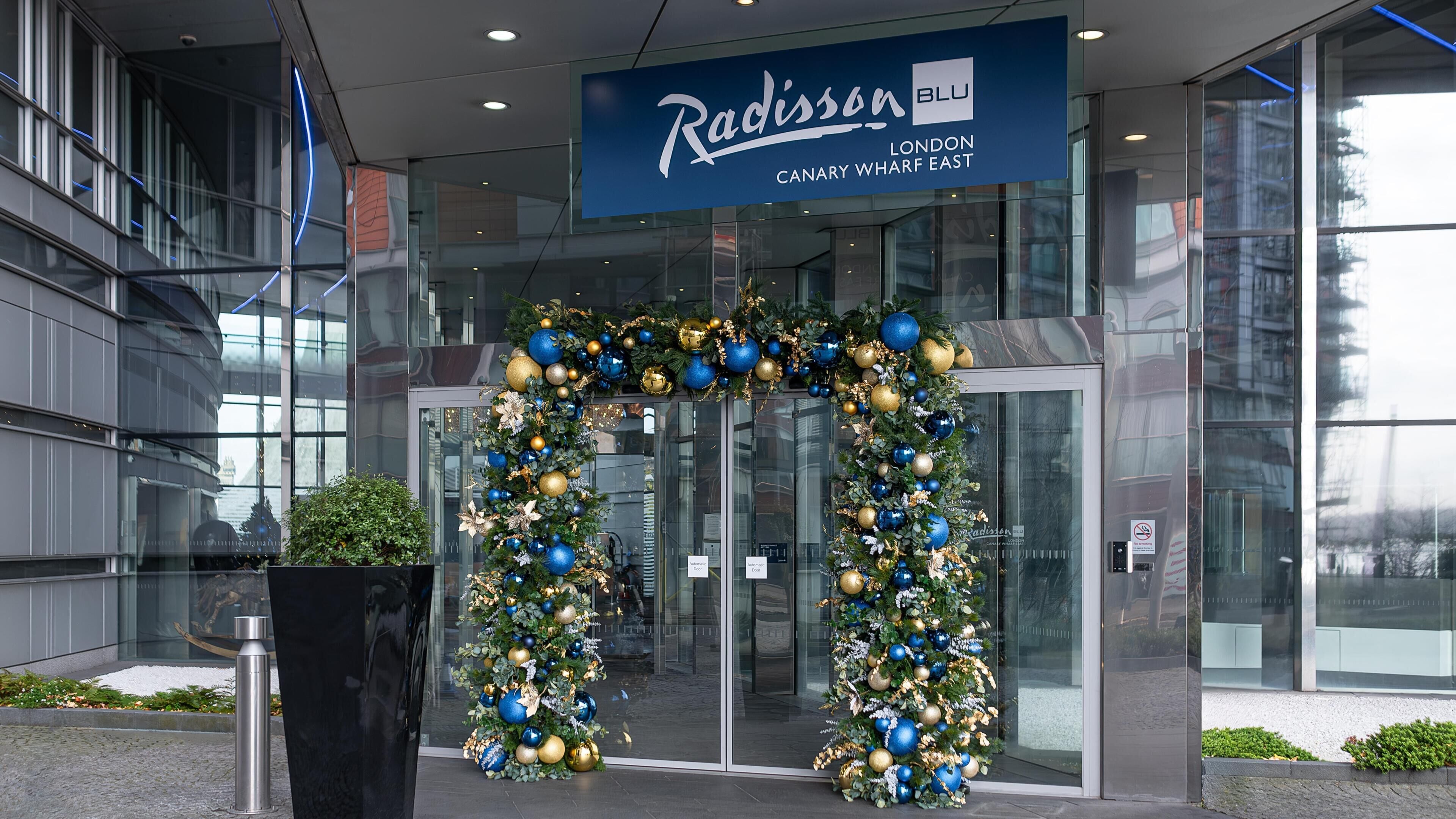A Radisson Blu London Canary Wharf East building entrance with a Christmas arch.