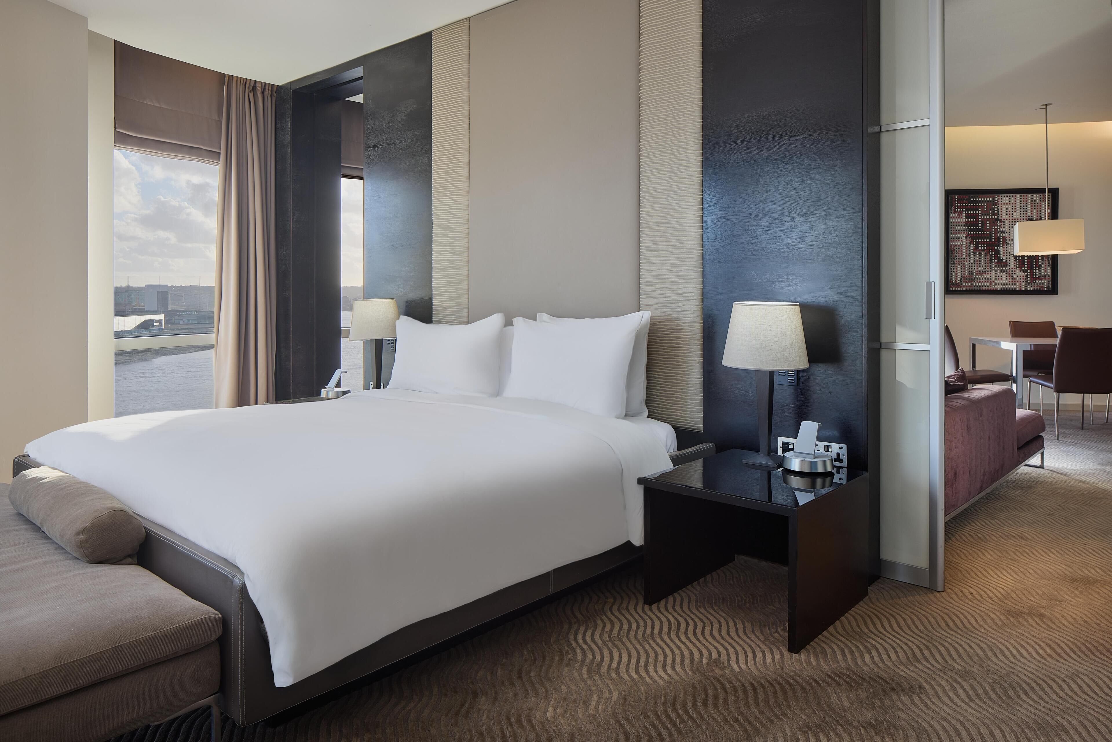 A hotel room with a large bed, a desk with a lamp, a sofa, and a view of a bridge.