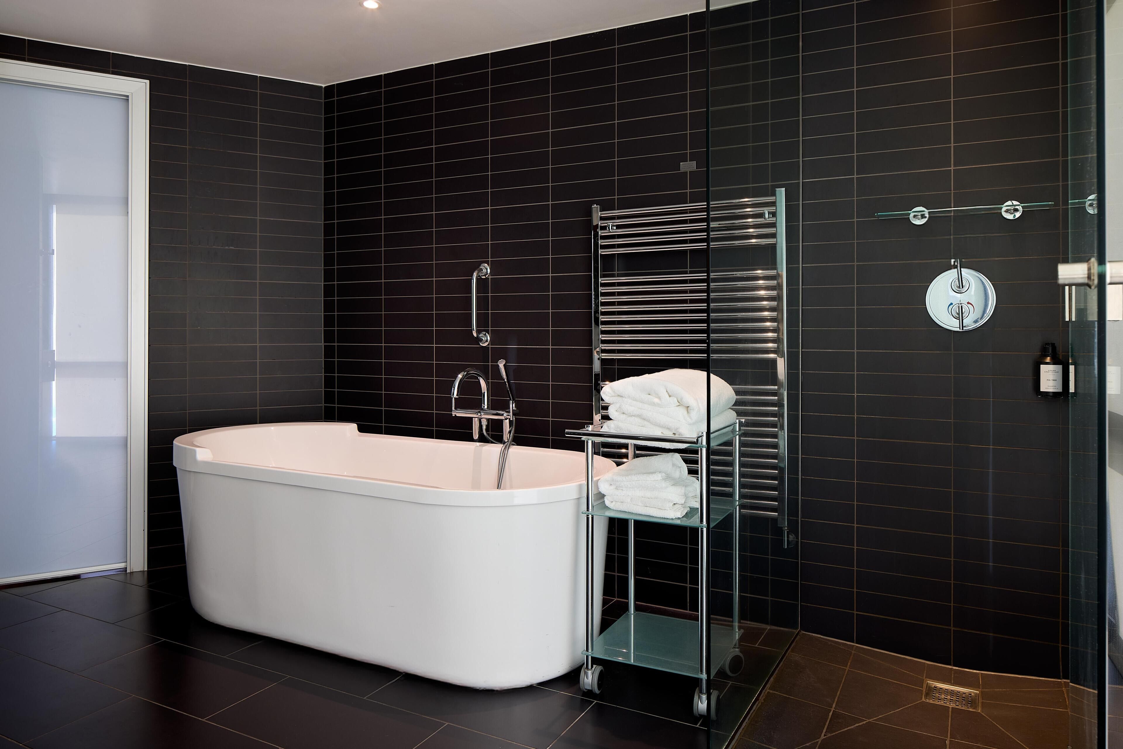 A modern bathroom with a freestanding bathtub, a glass shelf with towels, and a chrome towel rack.