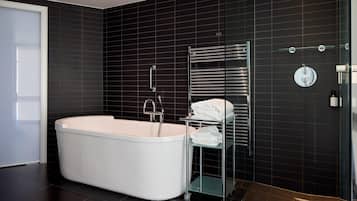 A modern bathroom with a freestanding bathtub, a glass shelf with towels, and a chrome towel rack.