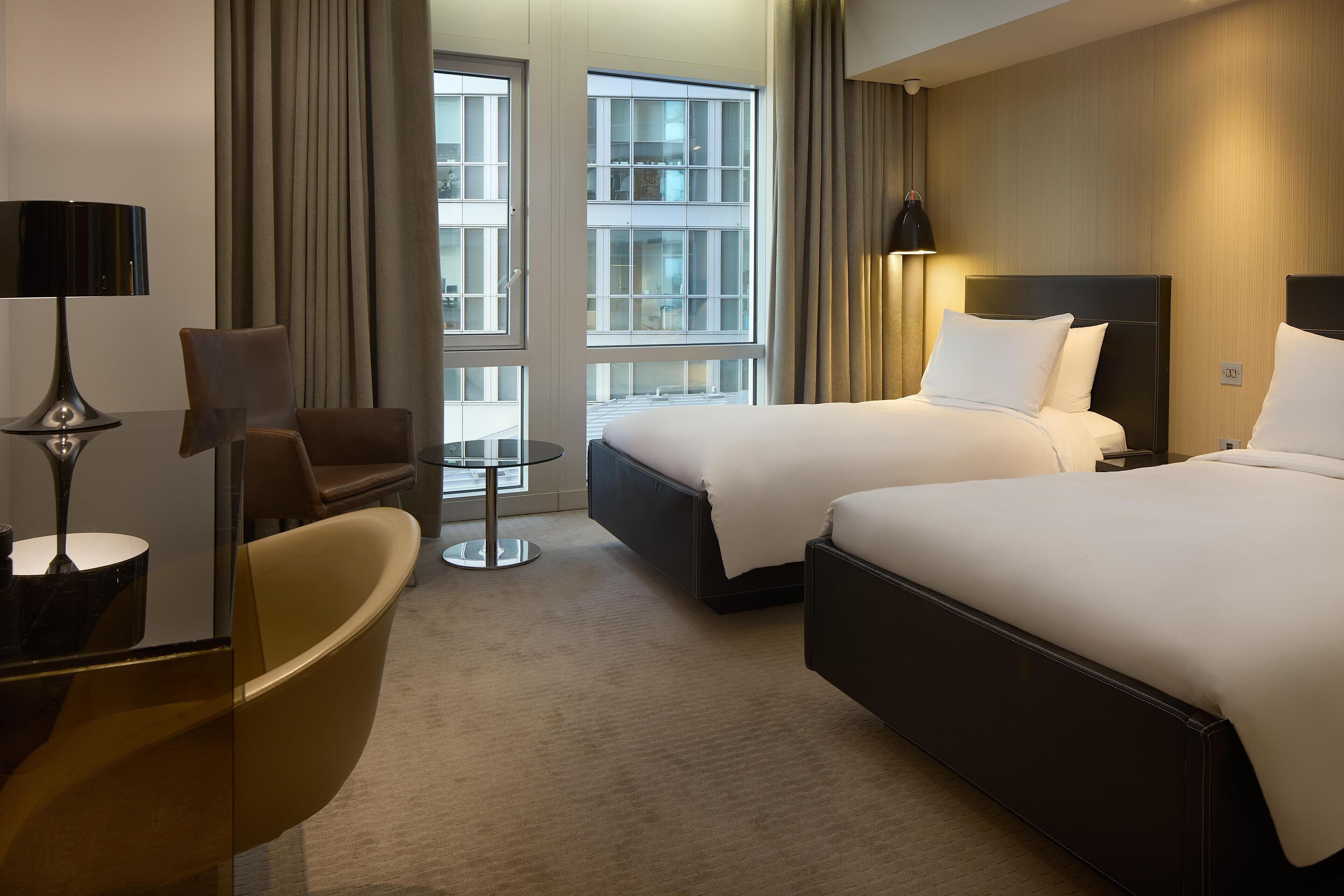 Une chambre d’hôtel avec deux lits, un bureau, une chaise et une vue sur l’extérieur.