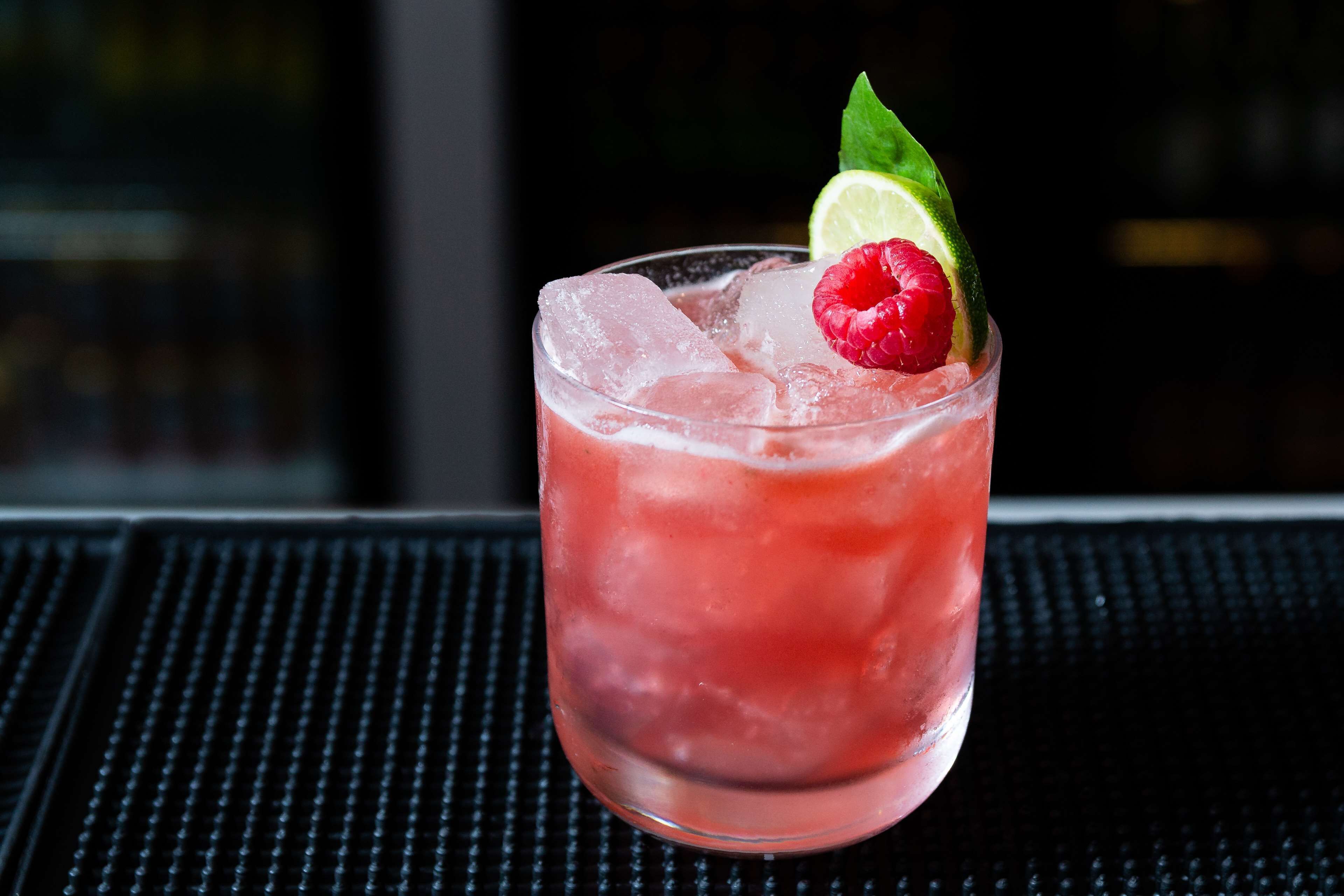 A glass of red beverage with ice cubes, garnished with a raspberry and a lime slice.
