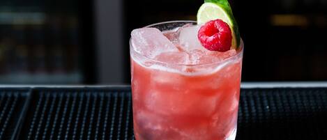 A glass of red beverage with ice cubes, garnished with a raspberry and a lime slice.