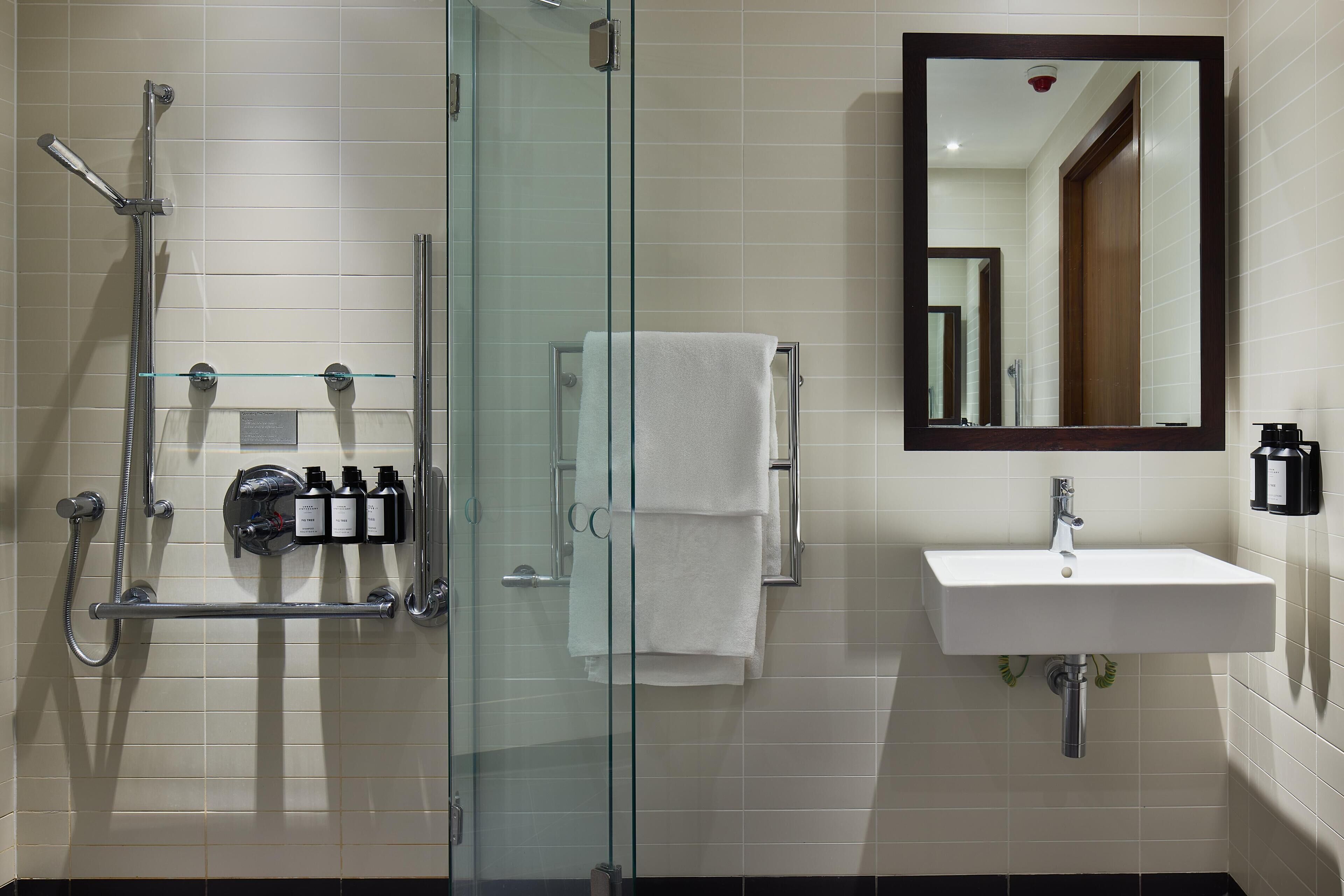 Un baño moderno con ducha de vidrio, un lavamanos blanco y un espejo grande.
